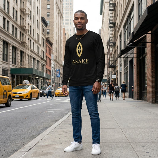 A man stands on a city sidewalk wearing a black long-sleeve crewneck shirt with a gold geometric logo and the word 'ASAKE' printed on the chest, paired with blue jeans and white sneakers. Yellow taxis and urban buildings are visible in the background.
