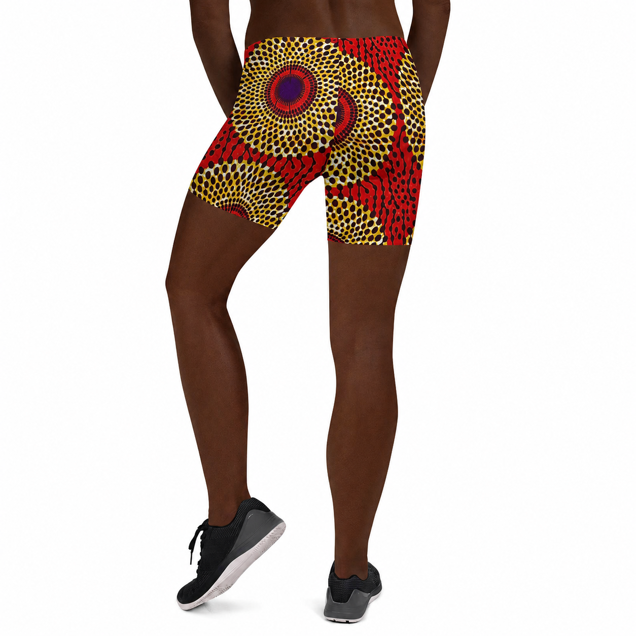 A person shown from the back wearing patterned athletic shorts with a bold African-inspired geometric print in red, yellow, black, and blue, paired with black sneakers against a plain white background.