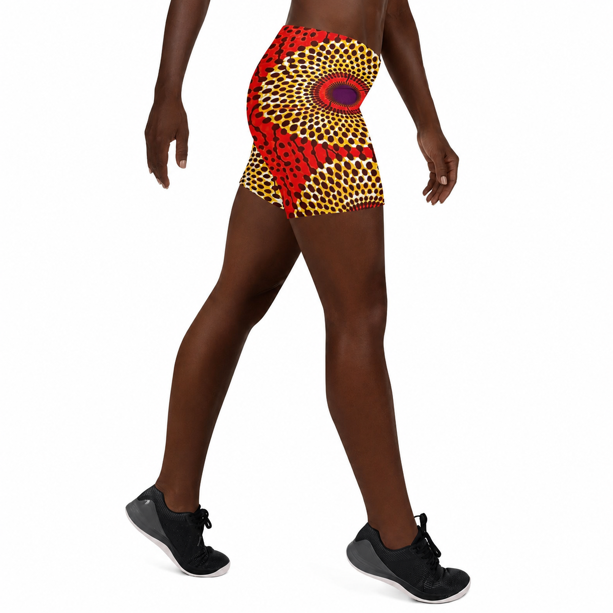 A model wearing high-waisted athletic shorts with a vibrant red, yellow, and black African wax print pattern, shown from the waist down against a plain white background.