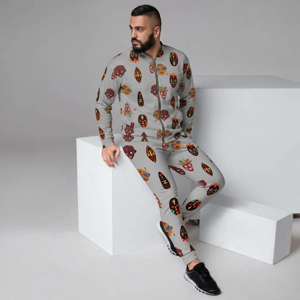 A man wearing a light gray zip-up hoodie and matching jogger pants with a colorful cartoon skull pattern, posing on white geometric display blocks in a studio setting.