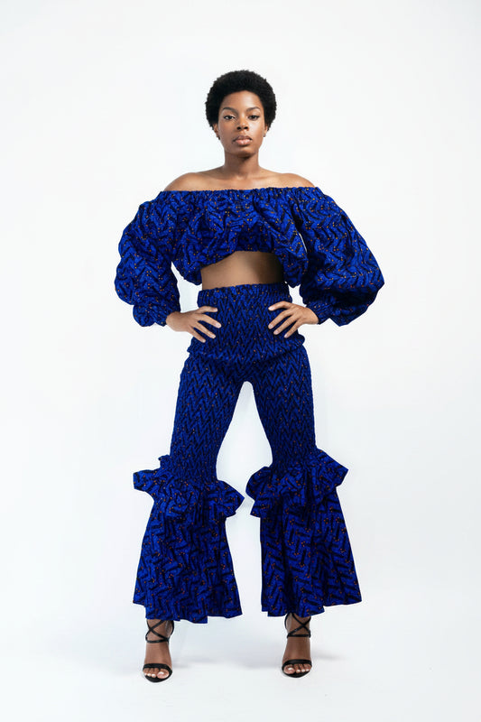 A model wearing an off-shoulder crop top and smocked two-step bell bottom set with blue and white African print design.