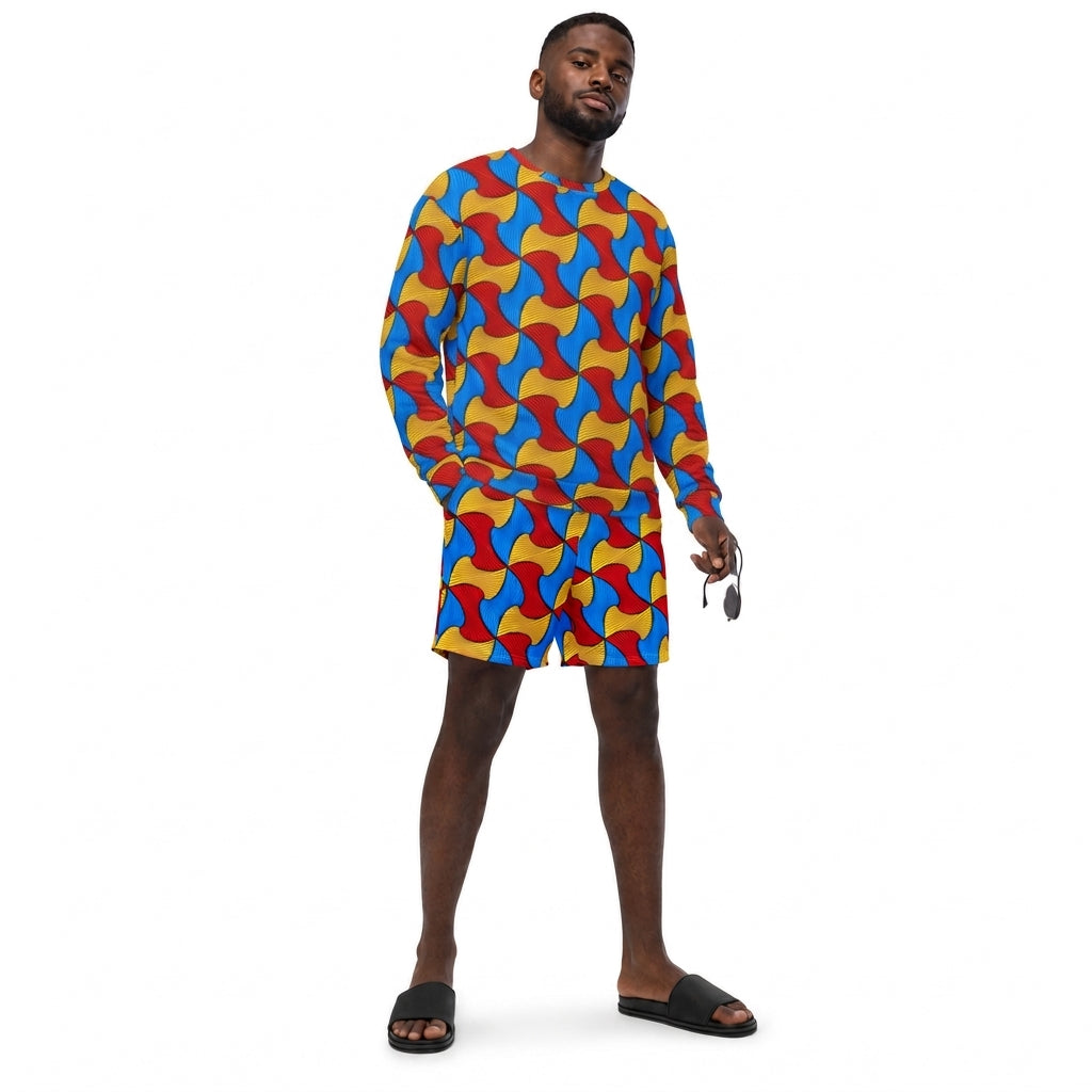 A man modeling a matching long-sleeve shirt and shorts set with a vibrant, repeating abstract wave pattern in red, blue, yellow, and orange, styled with black slide sandals against a plain white background.