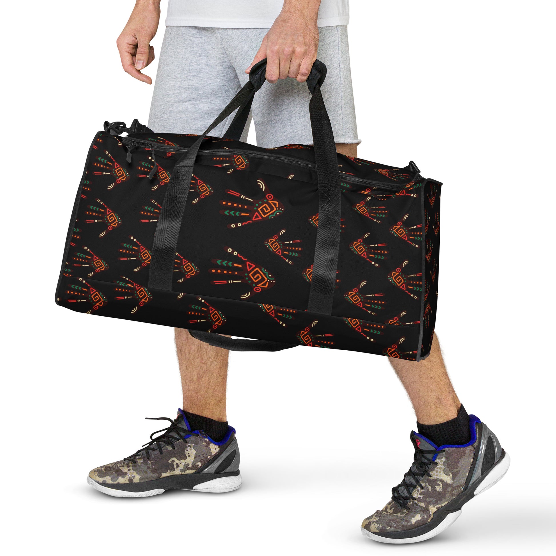 Man carrying black colored Duro Tribal Palm Print duffle bag by the dual short straps, showing the custom vibrant multicolor tribal palm print design.