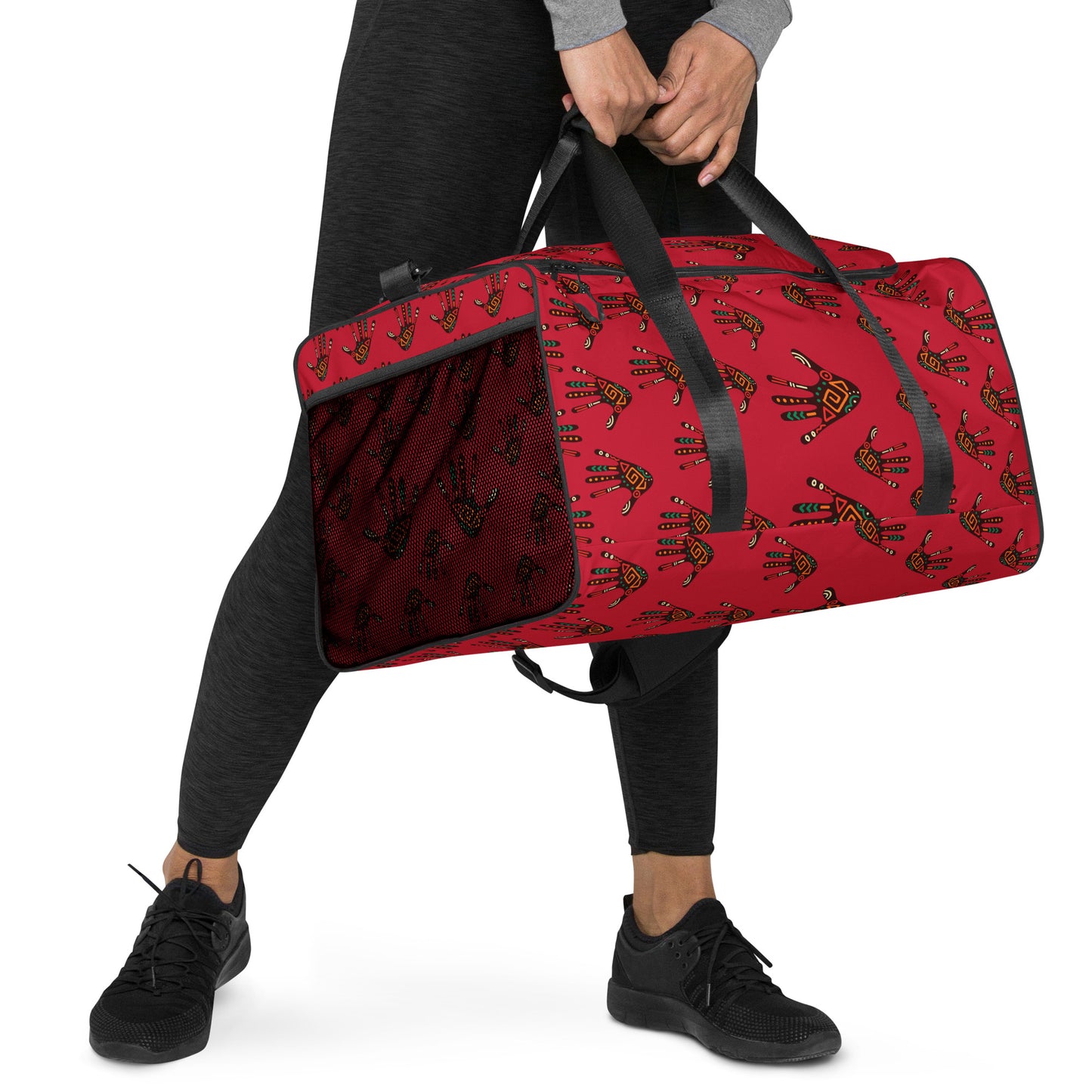  A woman holding the Duro Crimson Tribal Palm Print Duffle Bag by hand, with its dual shorter straps. 