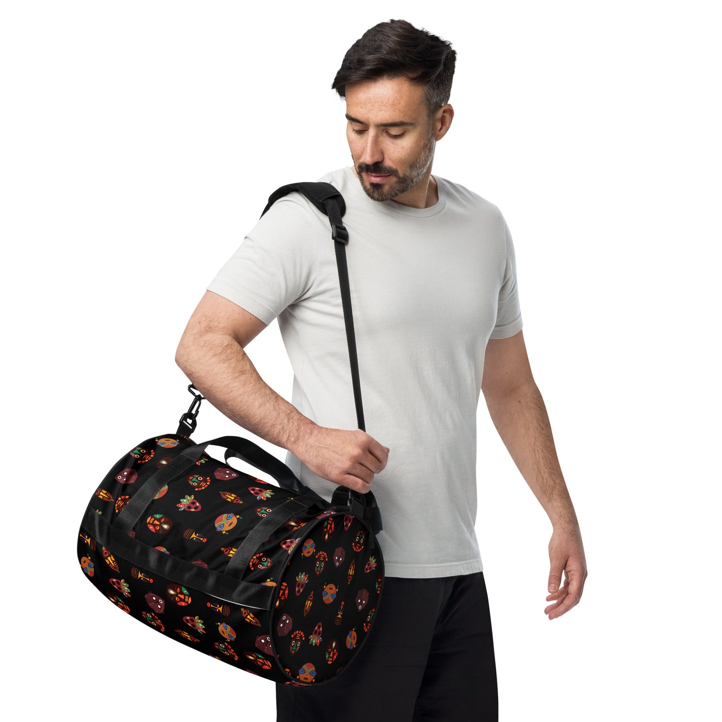 A man carrying the Chi Midnight Tribal Mask Overnight Gym Bag with the padded long straps on his shoulder; showcasing the circle-shaped left end and side view.