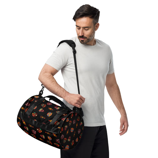 A man carrying the Chi Midnight Tribal Mask Overnight Gym Bag with the padded long straps on his shoulder; showcasing the circle-shaped left end and side view.