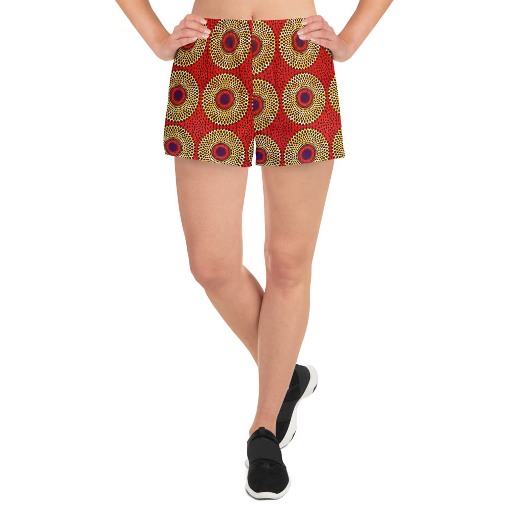 A woman wearing Rekiana African print athletic shorts with a geometric pattern in red, black, and yellow.