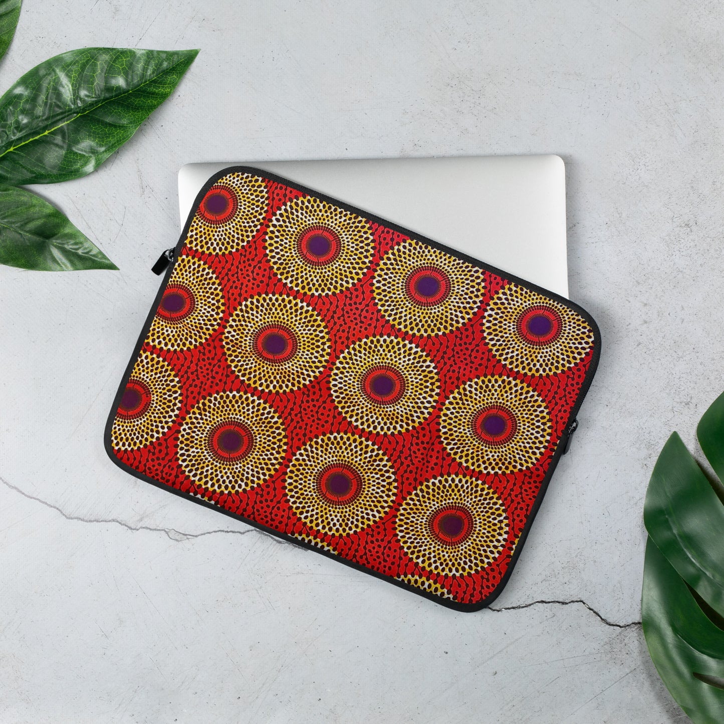 A vibrant 13 inch laptop sleeve with an African print design, featuring a top-loading zippered enclosure and two sliders, placed on a flat surface with a laptop inside.
