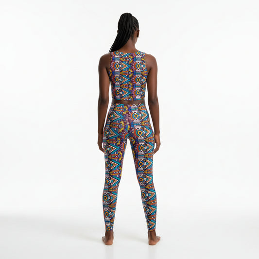 A woman stands with her back to the camera wearing a sleeveless, high-waisted one-piece jumpsuit with a vibrant geometric pattern in blue, red, orange, yellow, and white on a plain white studio background.