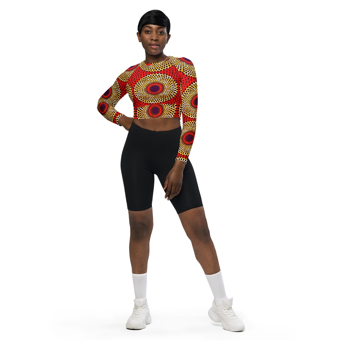 A woman wearing a long-sleeve crop top with a geometric pattern in red, yellow, and black colors, paired with black shorts.