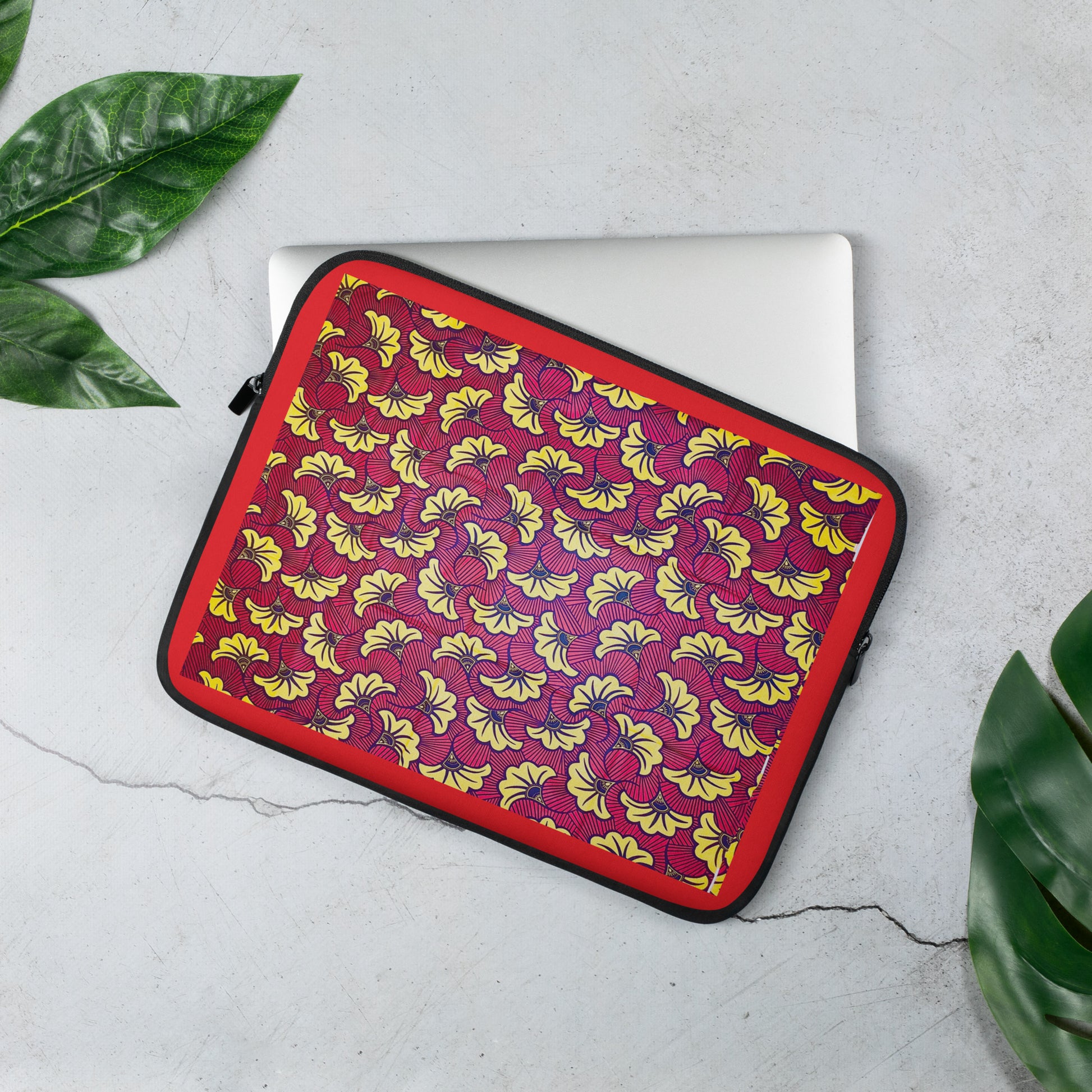 A 13 inch laptop sleeve with a floral African print pattern in the colors red, yellow, and black; displayed on a laptop.