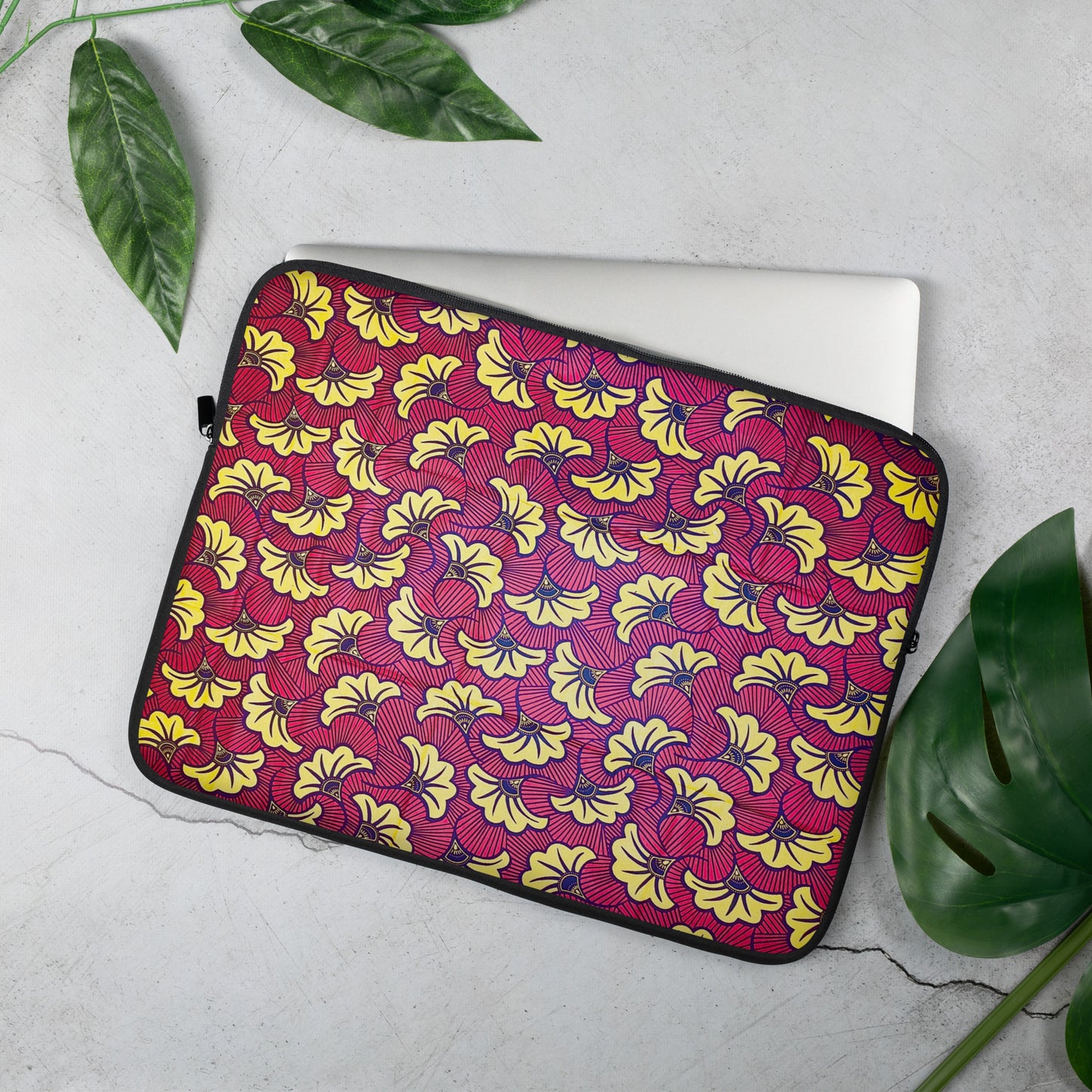 A 15 inch laptop sleeve with a floral African print pattern in the colors red, yellow, and black; displayed on a laptop.